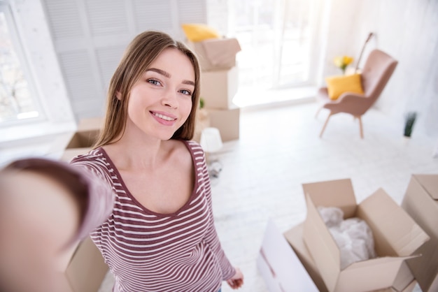 Huisverwarmende selfie. Mooie jonge vrouw die een selfie neemt die in een nieuwe flat is verhuisd en deze met haar vrienden wil delen