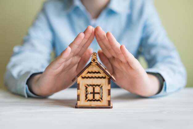 Huisverzekering en geld besparen op onroerend goed investeringen onroerend goed concept Zakenvrouw handen beschermen groot houten huis op tafel