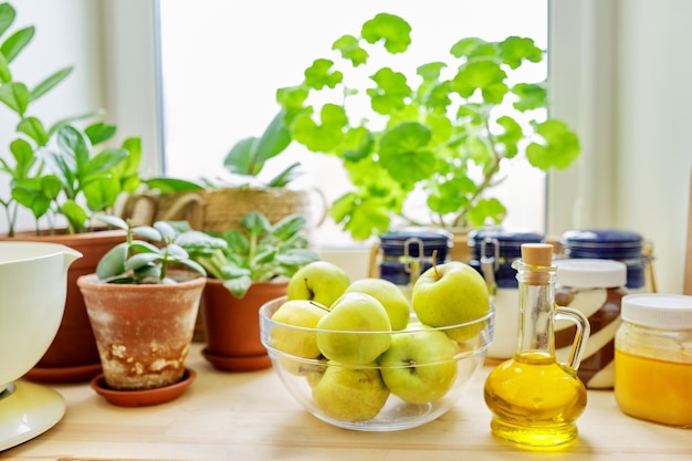 Huisvoorraadkast, voedselopslag, raam, houten tafel met huisplanten in potten, honing, chocoladepasta, kom groene appels, fles olijfolie