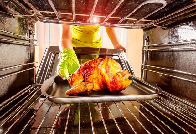 Foto huisvrouw bereidt gebraden kip in de oven, uitzicht vanaf de binnenkant van de oven. koken in de oven. dankdag.