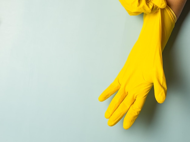 Huisvrouw die gele latex schoonmaakhandschoenen op blauwe achtergrond met kopieerruimte aantrekt