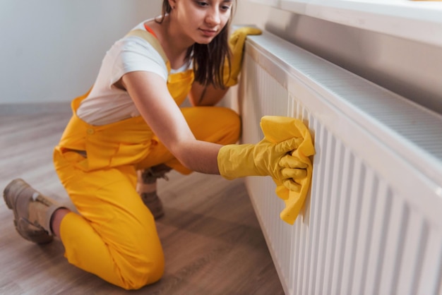 Huisvrouw in geel uniform werkt met raam- en oppervlaktereiniger binnenshuis Huisrenovatieconcept