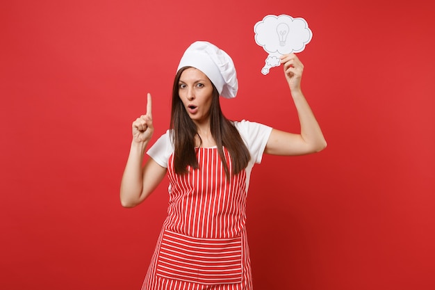 Huisvrouw vrouwelijke chef-kok of bakker in gestreepte schort wit t-shirt toque chef-koks hoed geïsoleerd op rode muur achtergrond. zelfverzekerde serieuze vrouw houdt het idee van een wolk gloeilamp. mock-up kopie ruimteconcept.