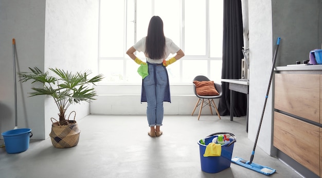 Huiswerk achteraanzicht van een jonge vrouw in gele rubberen handschoenen met vod en