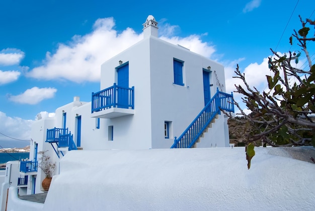 Huizen in mykonos, griekenland. witgekalkte gebouwen met blauw geschilderde ramen en deuren op zonnige hemel. typische architectuur en design. zomervakantie op mediterraan eiland. reizen en reis concept.