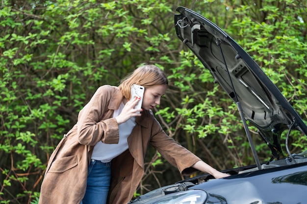 Hulpeloze vrouwenchauffeur die om hulp / assistentie roept die naar defecte auto kijkt, stopte langs de weg.