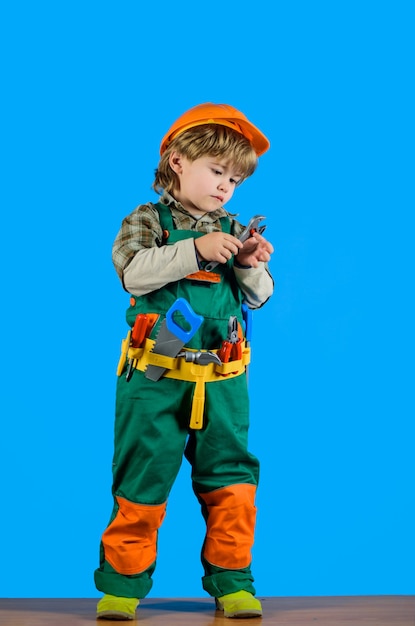 Hulpmiddelen voor het bouwen van een kleine jongen in een bouweruniform met een moersleutel voor een kinderspelbouwer in een helm