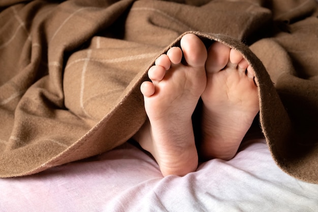 Human bare feet stick out from under the blanket