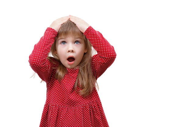 Foto emozioni umane. bambina in abito rosso sorpreso e scioccato. mani sulla testa, bocca aperta.