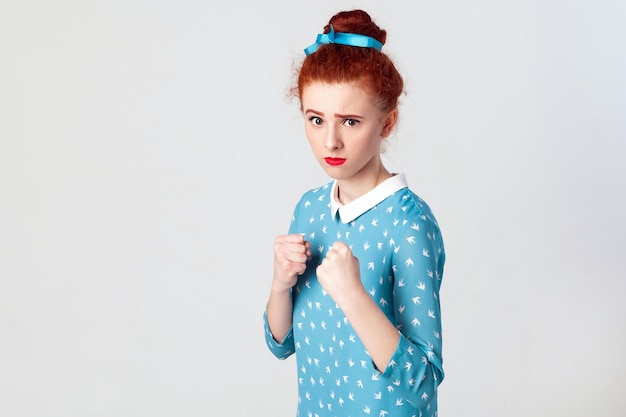 Human face expressions, emotions and feelings. Angry ginger girl, like a boxer, looking at camera. Isolated studio shot on gray background