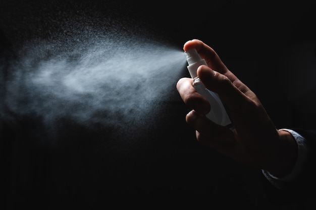 Human hand and antiseptic spray bottle on dark background. control epidemic prevention measures of coronavirus.