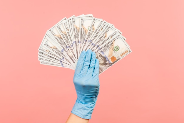 Mano umana in guanti chirurgici blu che tengono e mostrano un fan del dollaro americano in mano.