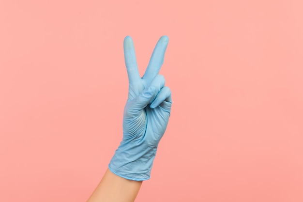 Human hand in blue surgical gloves showing victory, peace sign or number 2 with fingers.