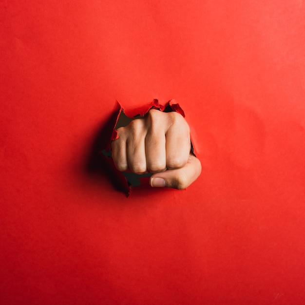 Human hand in a fist tearing red paper