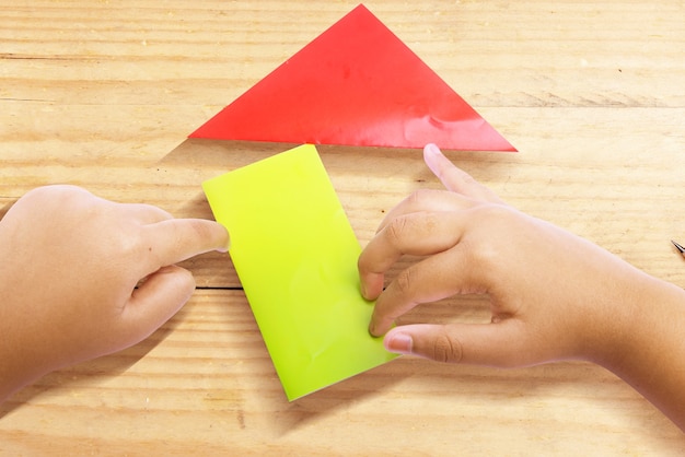 Human hand folding a colored paper wooden background