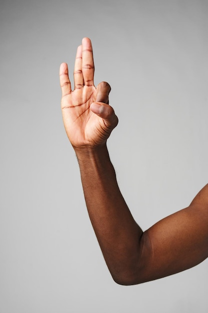 Human hand gesturing three fingers up against a neutral grey background