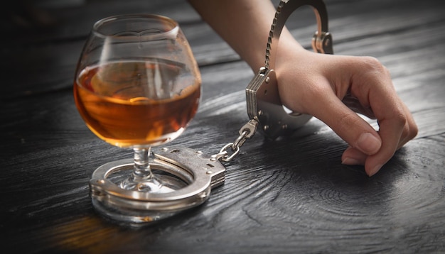 Human hand in handcuffs with a glass of cognac