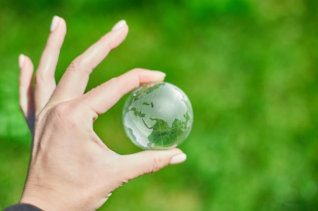 Человеческая рука держит стеклянный земной шар на фоне зеленой травы