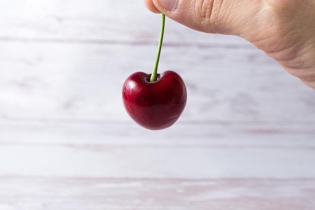 Human hand holding a cherry on a light background