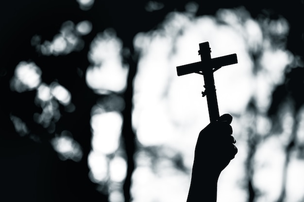 Human hand holding a christian cross with light bokeh background