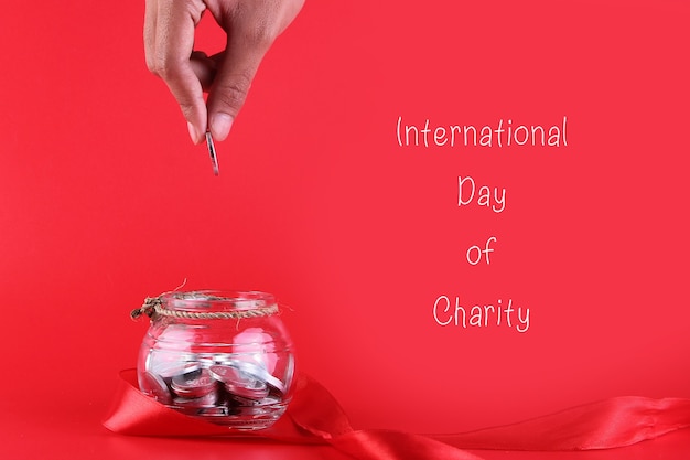 Human hand holding a coin to put in a transparent jar and decorated with a red ribbon around it