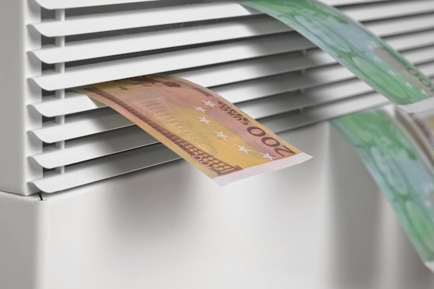 Human hand holding euro banknotes near electric heater radiator\
at home man pay money for heating expensive to heat energy saving\
rising cost of living global gas crisis paying cold season\
bills