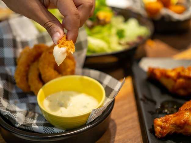 Human hand holding fish finger and dipping on mayonnaise sauce