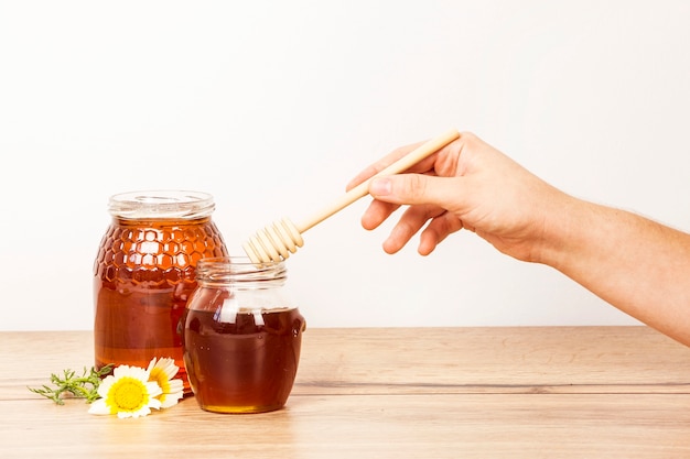 Photo human hand holding honey dipper from honey jar