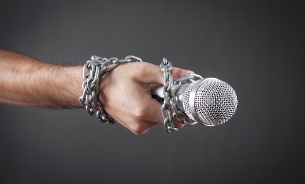 Human hand holding microphone tied with chains.