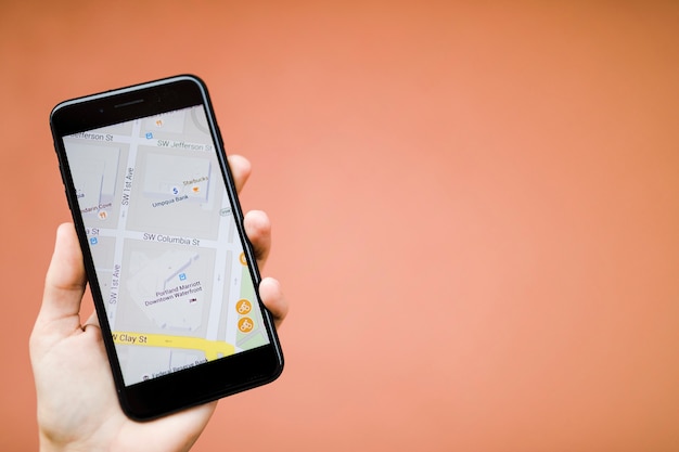 Mano umana che tiene il telefono cellulare con navigazione gps mappa su sfondo arancione