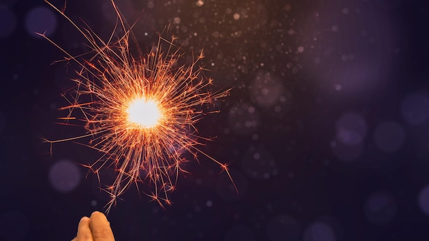 Human hand holding sparkler with colorful blurred light for the background