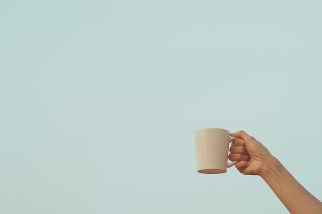 Photo human hand holding white coffee cup up to the air with blue sky background