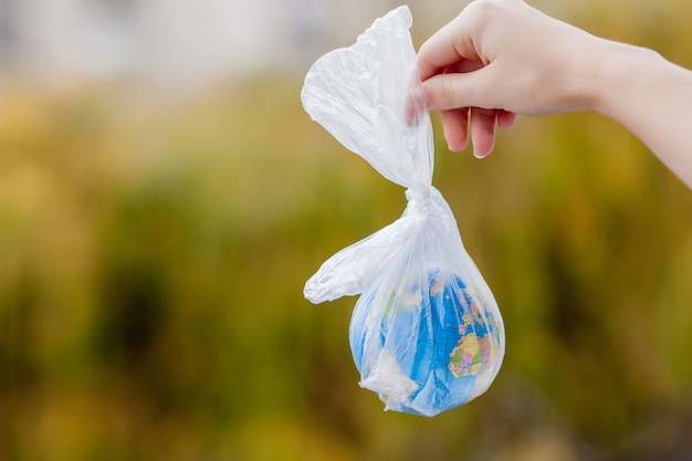 人間の手は、地球をビニール袋に入れて保持しています。プラスチック破片による汚染の概念。温室効果による地球温暖化。