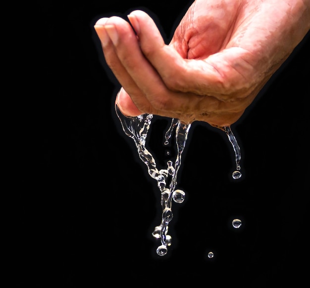 The human hand holds water with his hands and the water drops\
below. the purity of the water.