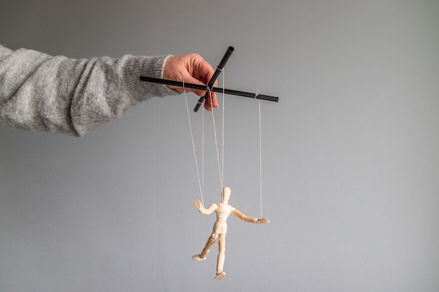 Photo the human hand holds a wooden doll on the clothesline on a gray background with place for text. power metaphor concept