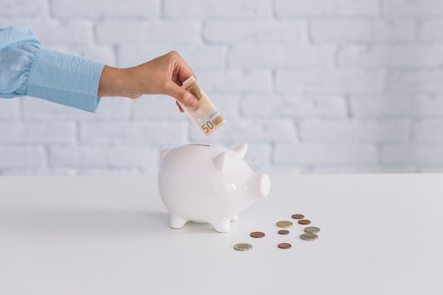 Human hand inserting fifty euro banknote in piggybank on desk