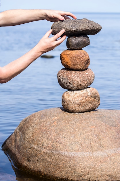 Human hand making stack of large round stones near the water