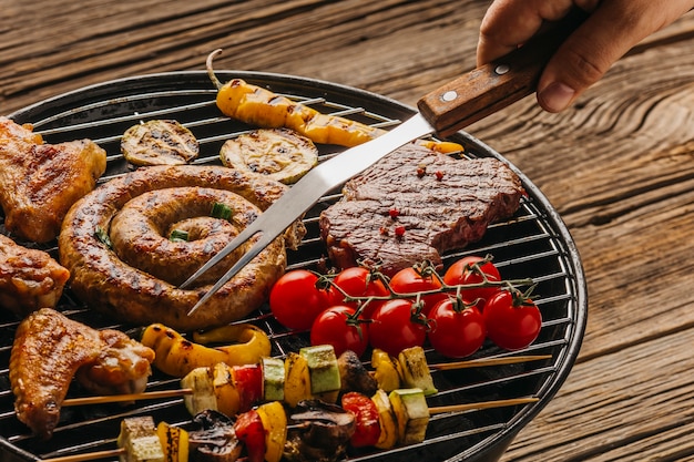 Human hand preparing grilled meat and sausages on barbecue