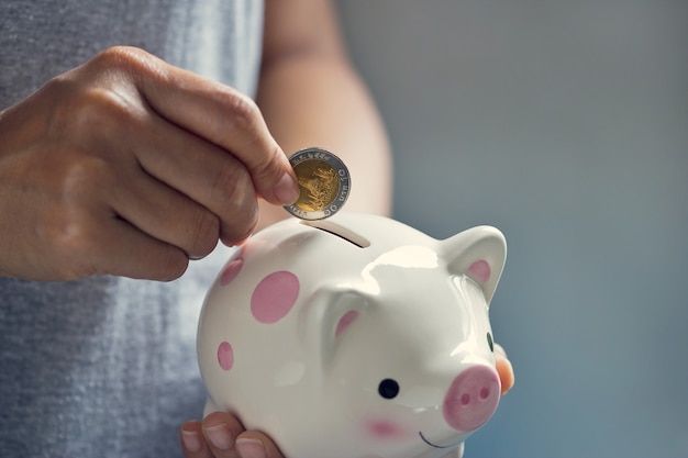 Human hand putting coin into piggy bank 