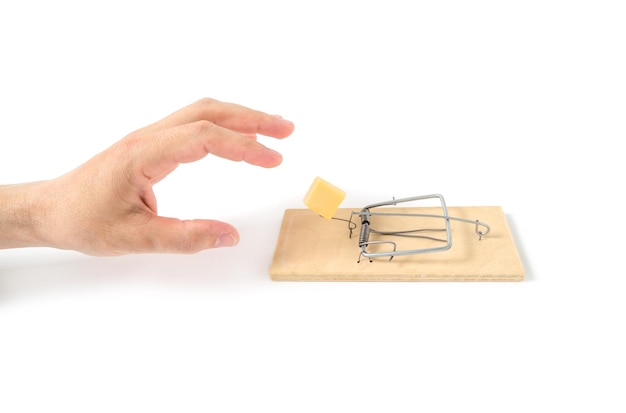 Human hand reaches for cheese mousetrap on white backgroundClose up