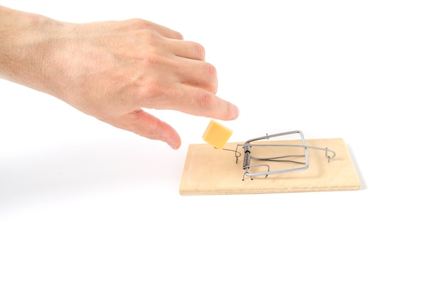 Human hand reaches for cheese mousetrap on white backgroundClose up