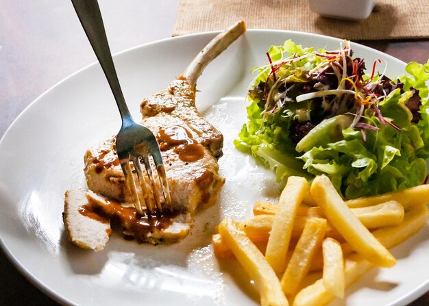 Human hand using knife cutting grilled pork chops steak Close up in restaurant Pork chop steak with salad and french fries