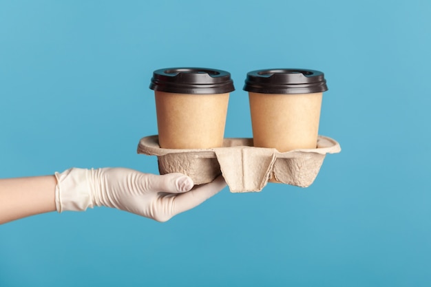 Human hand in white surgical gloves holding and showing cup of hot takeaway mug drink in hand.