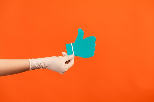 Human hand in white surgical gloves holding and showing like or thumbs up paper shape sign