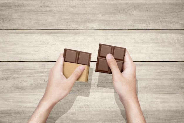 Human hand with the chocolate bar with table background