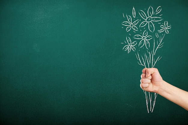 Human hand with drawn flowers on green chalkboard