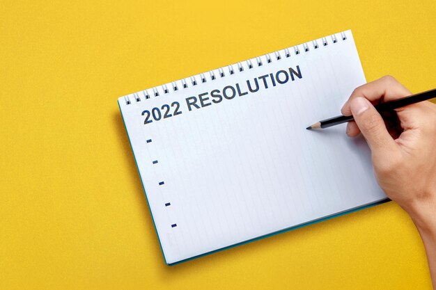 人間の手が2022年の解像度のリストをノートブックに書き込みます。 2022年の決議。2022年明けましておめでとうございます。