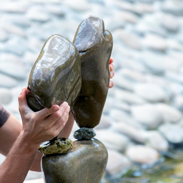 人間の手が水の上に石のケアンを作ります。バランスと瞑想