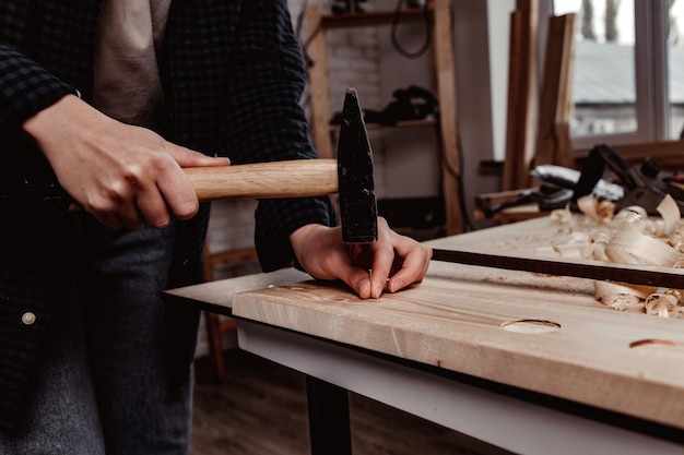 Human hands hammer nail into a wooden bar