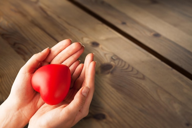 Human hands holding a heart on wooden desk